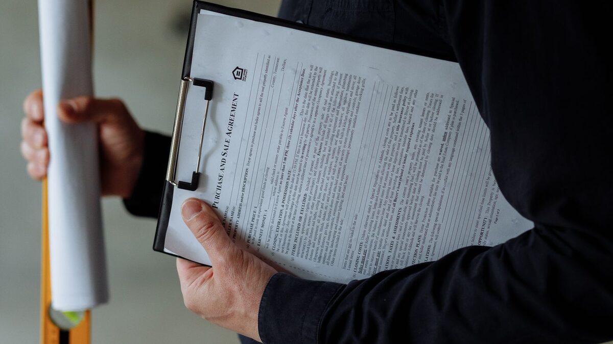 Persoană ținând planuri și un clipboard cu un document