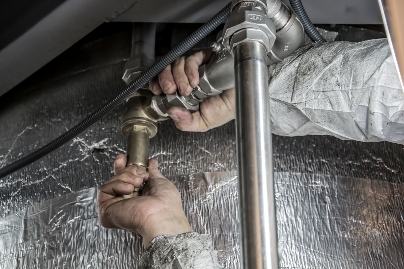 Mâinile unui instalator strângând fitingurile unei conducte de apă